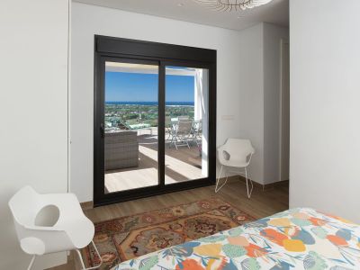 Dormitorio con edredón colorido, suelo de madera y acceso directo a una terraza privada. Grandes puertas correderas enmarcan vistas panorámicas al mar y la costa, maximizando la luz natural.