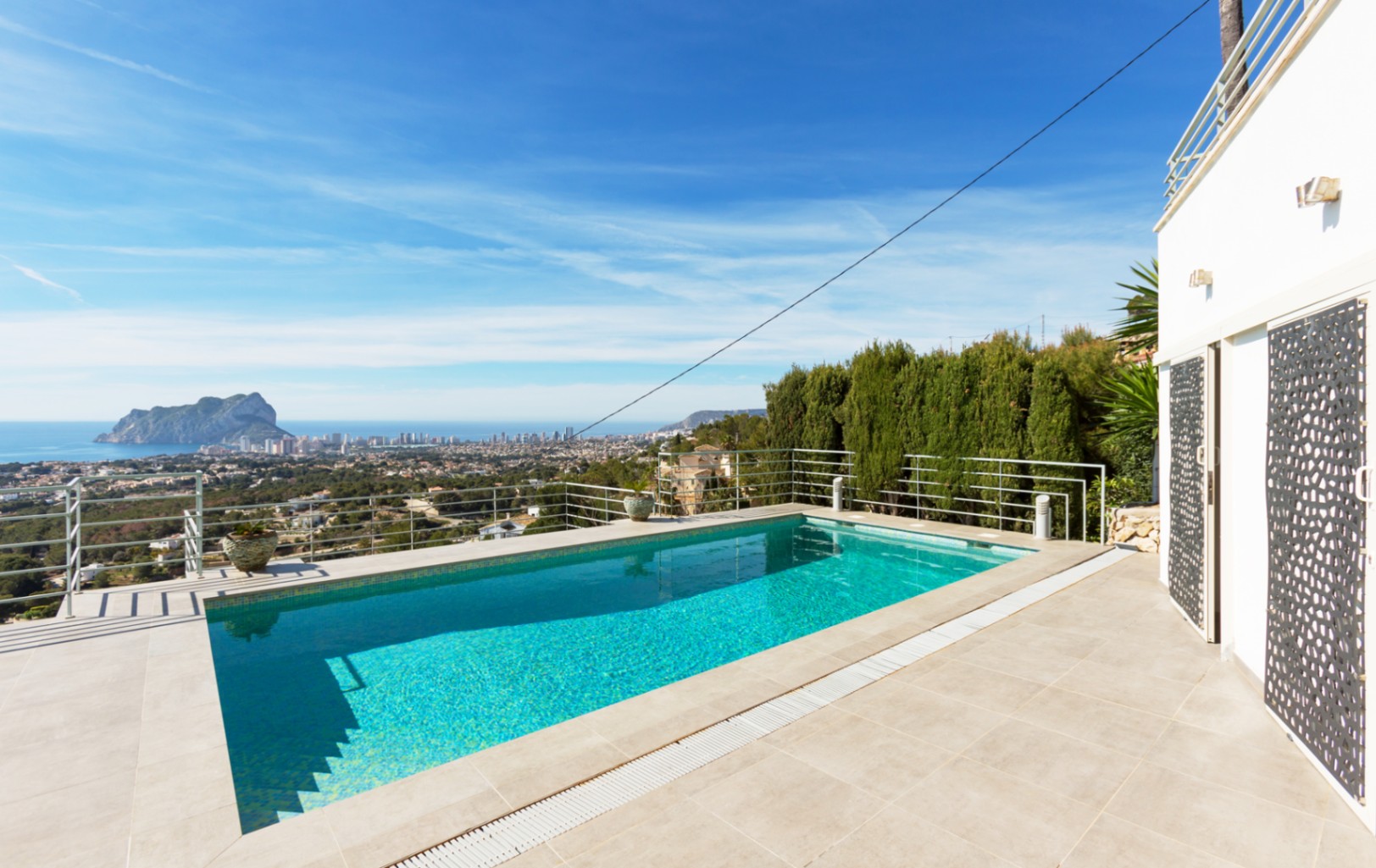 Piscina exterior rectangular con terraza de gres y barandilla metálica, con vistas panorámicas al mar Mediterráneo y al Peñón de Ifach en Calpe.