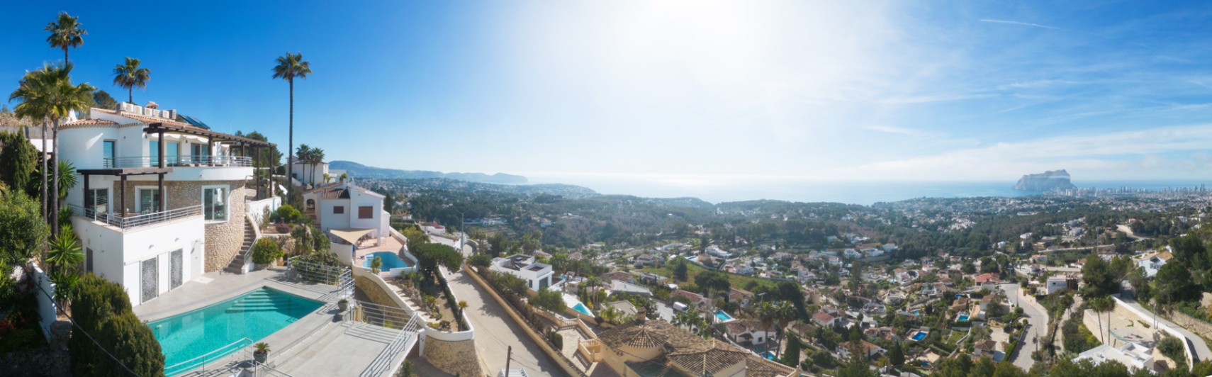 Vista panorámica de una villa mediterránea con piscina privada, fachadas de piedra y amplias terrazas con vistas despejadas a la costa y al Peñón de Ifach.