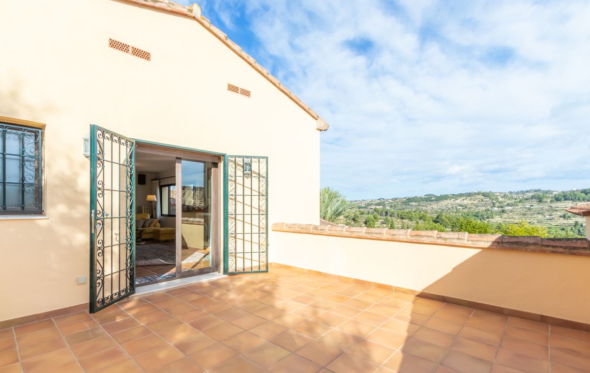 Terraza elevada con suelos de terracota y rejas de hierro forjado verde, con vistas panorámicas al valle y las colinas circundantes.