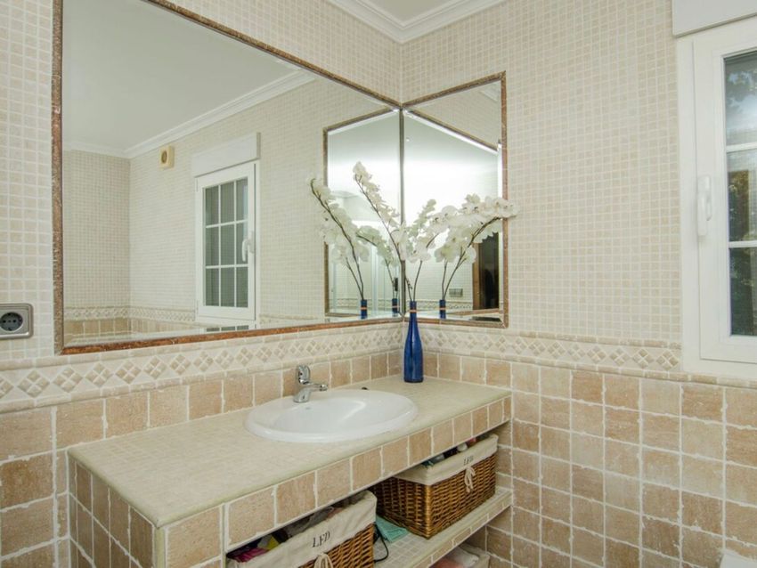 Baño con lavabo integrado sobre encimera de azulejos beige. Destacan los espejos de pared en esquina y los detalles de mosaico y cenefa en las paredes. Baño con lavabo integrado sobre encimera de azulejos beige. Destacan los espejos de pared en esquina y los detalles de mosaico y cenefa en las paredes.
