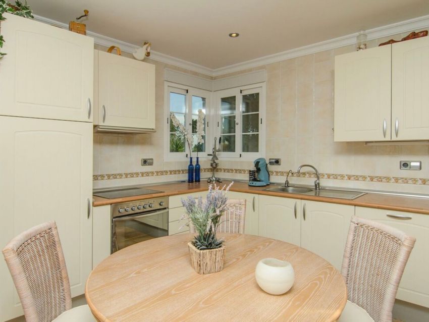 Cocina de estilo rústico con armarios color crema, encimeras de madera y una luminosa zona de desayuno con mesa redonda junto a la ventana esquinera. Cocina de estilo rústico con armarios color crema, encimeras de madera y una luminosa zona de desayuno con mesa redonda junto a la ventana esquinera.