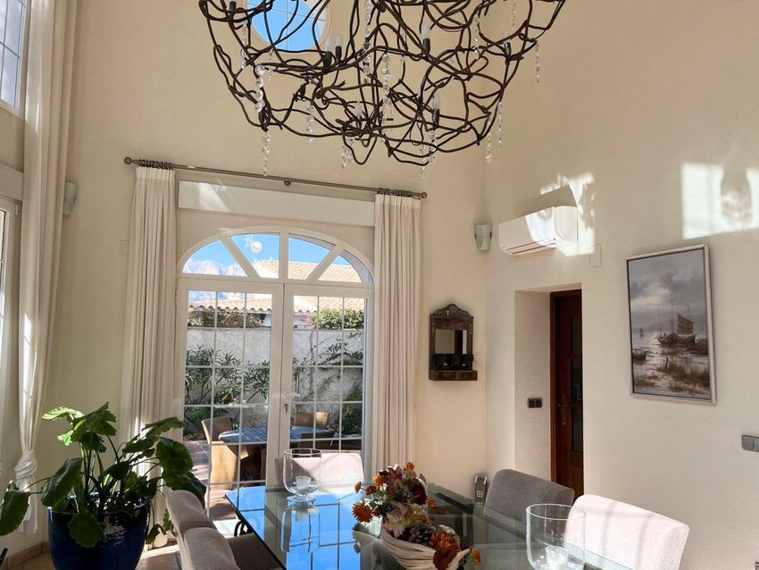 Comedor luminoso con mesa de cristal y sillas tapizadas, destacando las puertas francesas arqueadas que conectan con un patio exterior. Techos altos con una lámpara de diseño. Comedor luminoso con mesa de cristal y sillas tapizadas, destacando las puertas francesas arqueadas que conectan con un patio exterior. Techos altos con una lámpara de diseño.