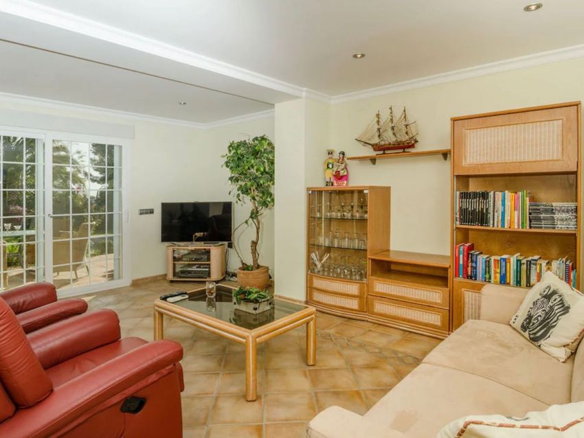 Salón con suelo de baldosas, amplias puertas correderas de cristal con acceso al jardín y un mueble modular de madera que integra TV, vitrina y estanterías. Salón con suelo de baldosas, amplias puertas correderas de cristal con acceso al jardín y un mueble modular de madera que integra TV, vitrina y estanterías.