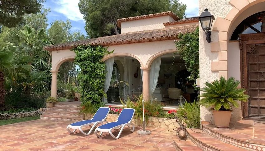Terraza exterior con suelo de baldosas de terracota y dos tumbonas, frente a una elegante logia acristalada con arcos y cortinas ligeras. Rodeada de exuberante vegetación mediterránea, ofrece un ambiente sereno. Terraza exterior con suelo de baldosas de terracota y dos tumbonas, frente a una elegante logia acristalada con arcos y cortinas ligeras. Rodeada de exuberante vegetación mediterránea, ofrece un ambiente sereno.