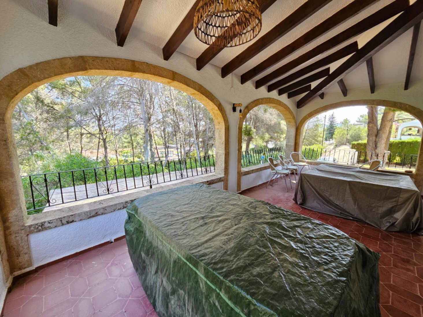 Terraza cubierta con arcos de piedra tosca, vigas de madera oscura y suelo de terracota con vistas al entorno boscoso.