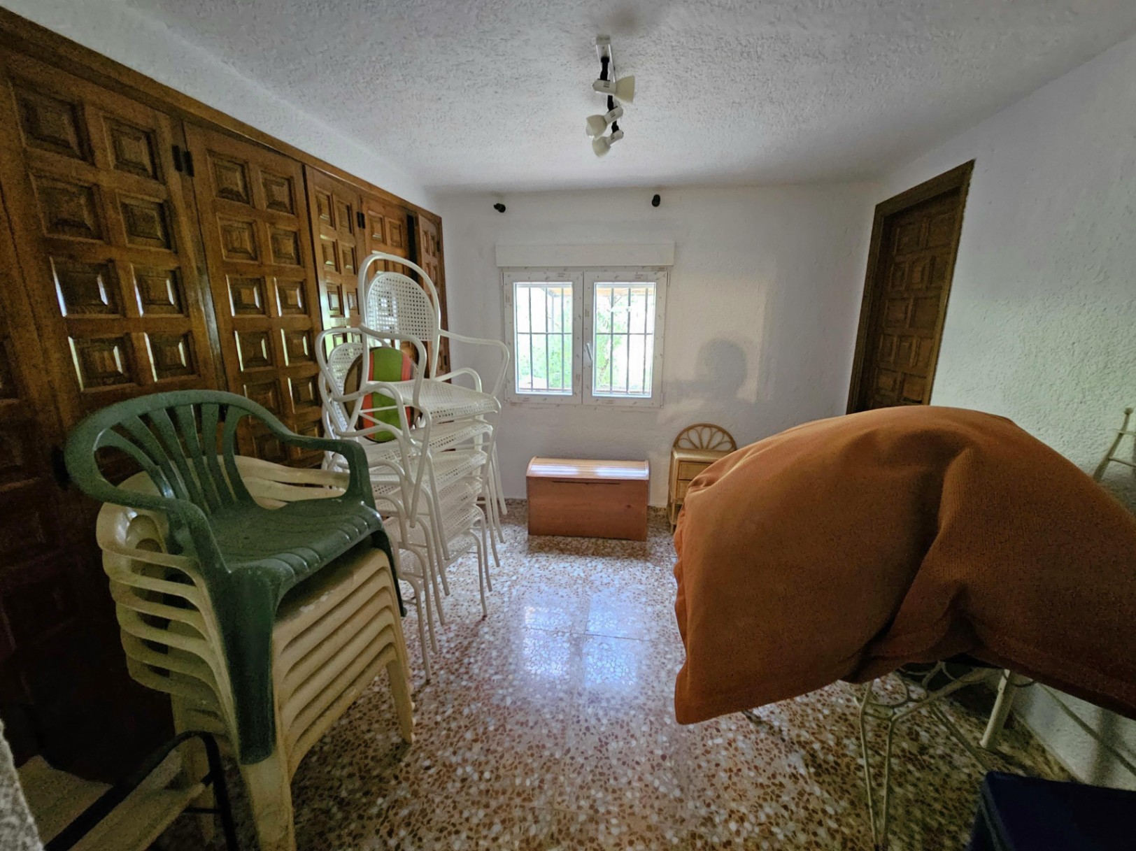 Trastero con armarios empotrados de madera tallada, suelos de terrazo y ventana con rejas de seguridad para mayor protección.