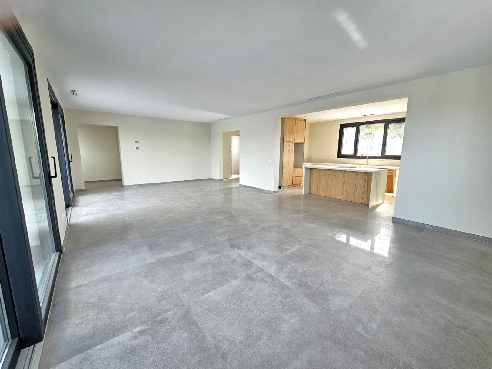 Amplia sala de estar con suelos de gres porcelánico y cocina abierta con isla central de madera clara.