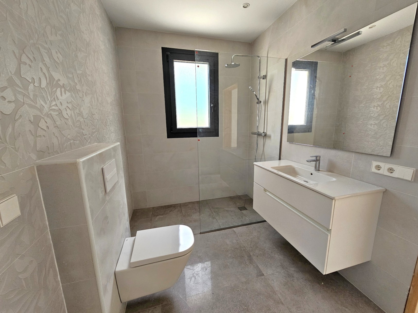 Cuarto de baño moderno con ducha a ras de suelo, lavabo suspendido blanco y pared con diseño floral.