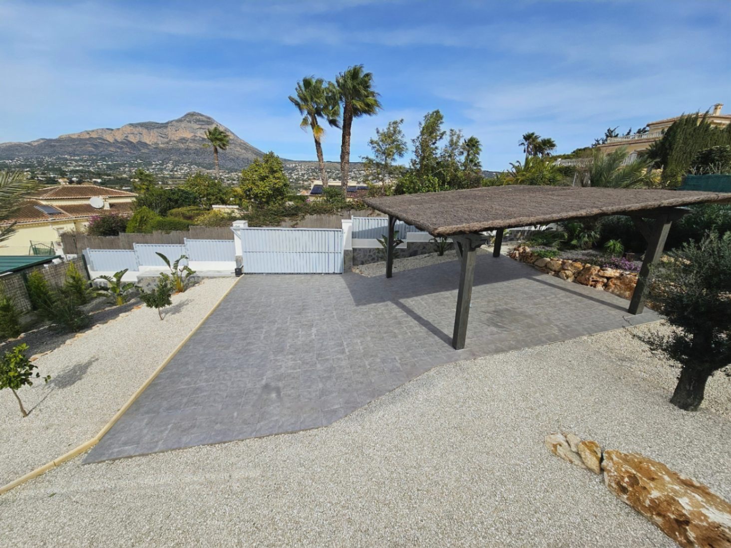 Entrada a la villa con portón eléctrico, zona de aparcamiento cubierta con pérgola y vistas al Montgó.