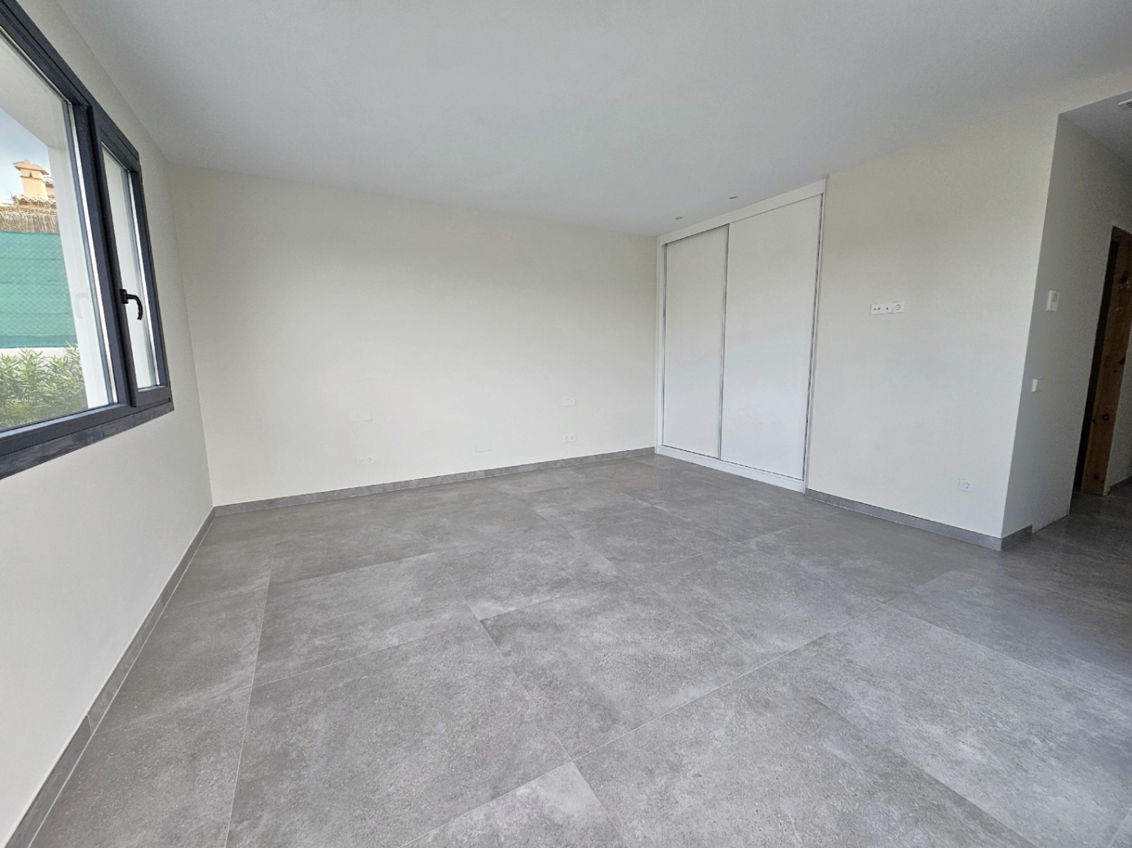 Habitación luminosa con suelo de gres gris y armario empotrado blanco con puertas correderas.