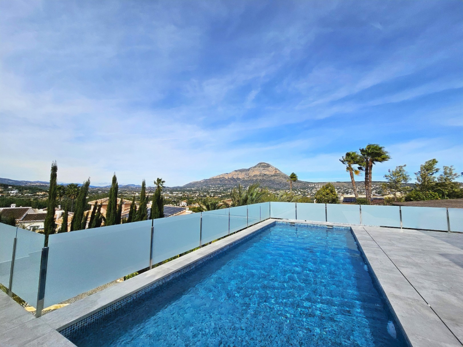 Vista de la piscina con mosaicos azules y barandilla de cristal, con vistas al monte Montgó.