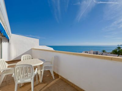 Amplia terraza con mobiliario de exterior y vistas panorámicas al mar Mediterráneo, bajo un cielo azul claro. El suelo es de baldosas claras y la barandilla es blanca.