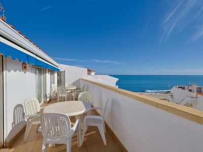 Amplia terraza privada con mobiliario de exterior blanco, toldo azul y vistas panorámicas al mar Mediterráneo bajo un cielo despejado.