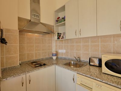 Cocina compacta con encimera de efecto granito, salpicadero de azulejos beige y electrodomésticos esenciales, incluyendo placa y fregadero de acero.