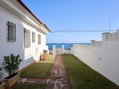 Jardín exterior con camino de losas de piedra que conduce a un portón con vistas directas al mar Mediterráneo. La casa blanca presenta rejas de forja y tejado de teja.