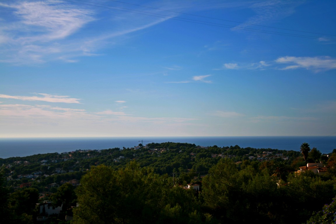 Vista panorámica de Benimeit, Moraira, con el mar Mediterráneo al fondo y cielo azul con nubes.