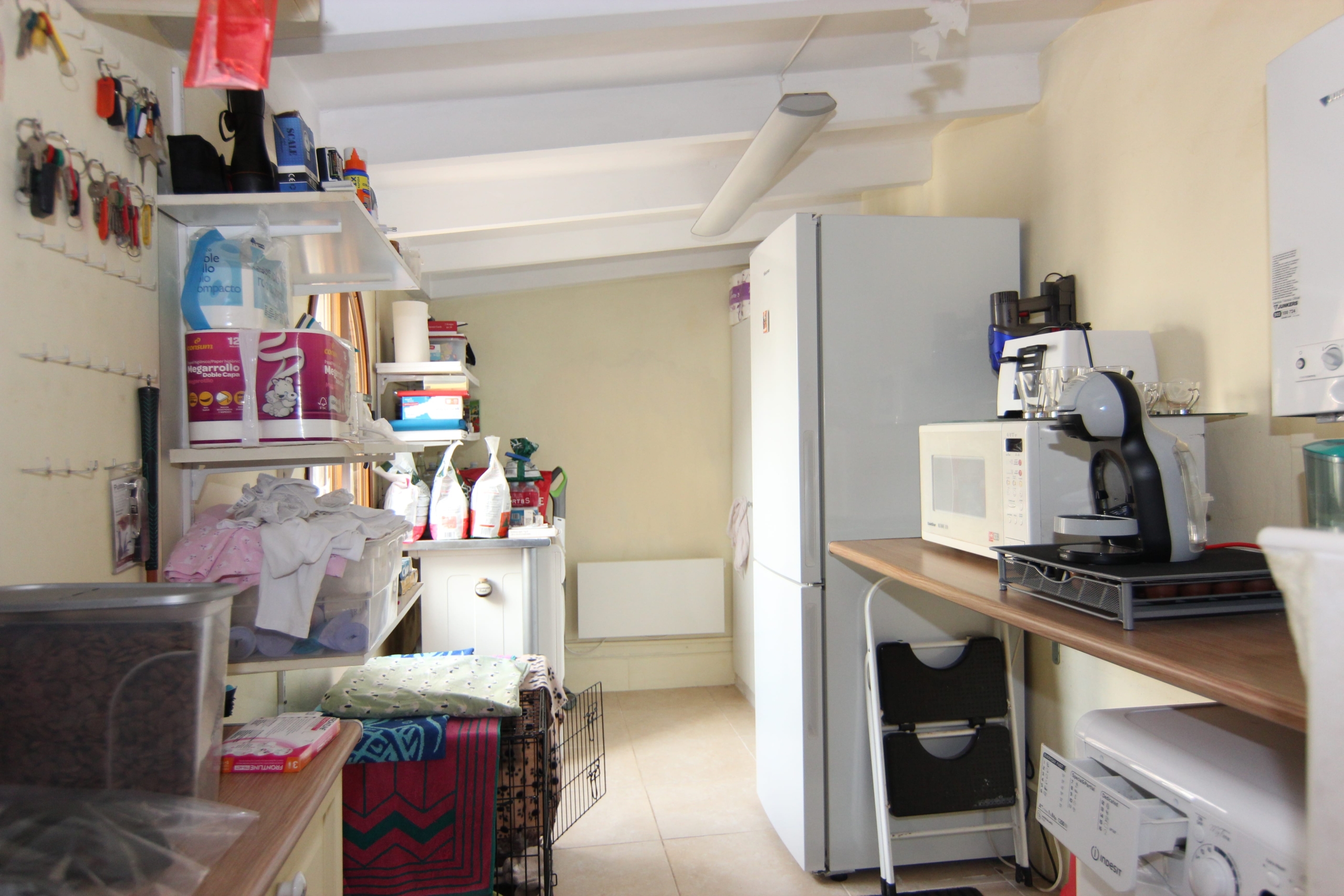 Detalles del lavadero: estanterías con productos, nevera blanca y electrodomésticos sobre encimera.