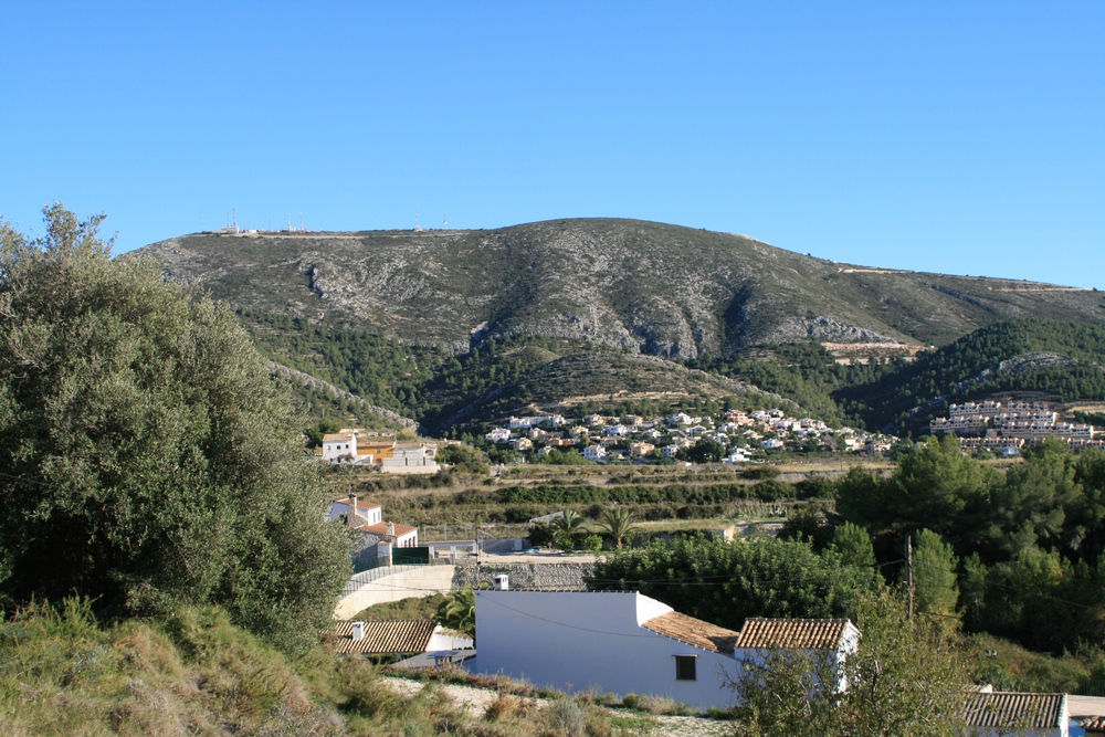 Vista del paisaje rural de Benitachell con casas de tejas y montaña al fondo. Vista del paisaje rural de Benitachell con casas de tejas y montaña al fondo.