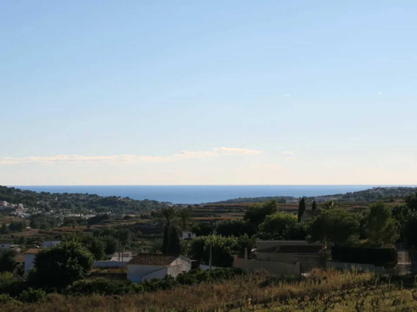 Vista panorámica del terreno con casas de tejas y el Mediterráneo al fondo bajo un cielo azul despejado. Vista panorámica del terreno con casas de tejas y el Mediterráneo al fondo bajo un cielo azul despejado.
