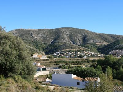 Vista del paisaje rural de Benitachell con casas de tejas y montaña al fondo.