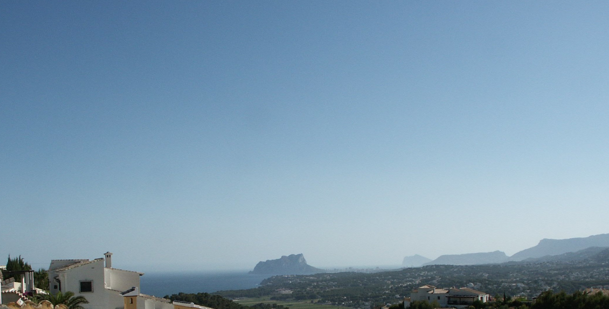 Vista panorámica de Benitachell con el Peñón de Ifach al fondo, bajo un cielo despejado.