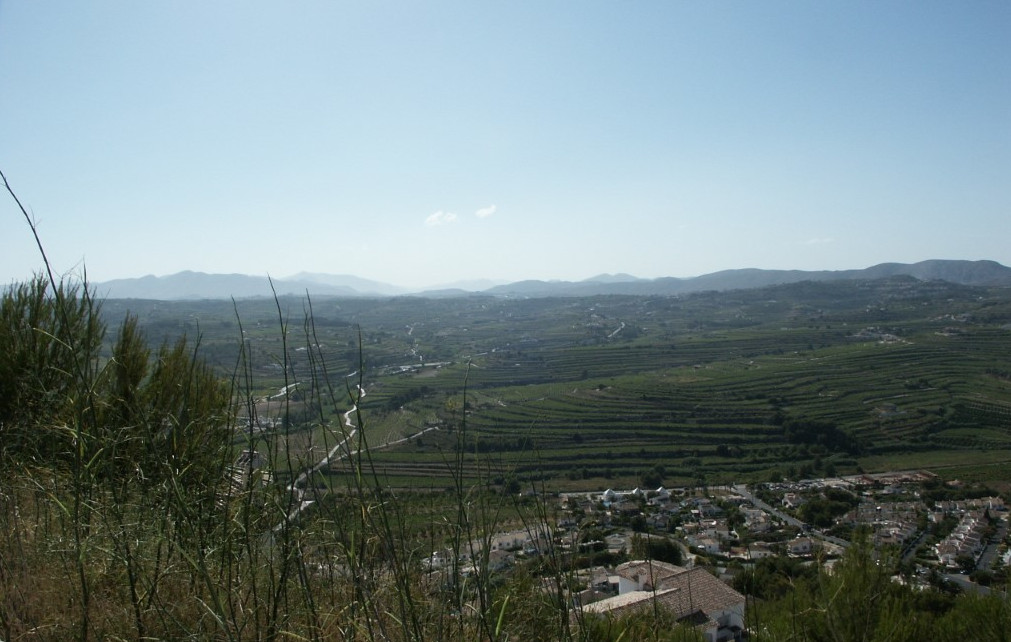Vista panorámica de Benitachell con terrazas agrícolas y montañas al fondo.