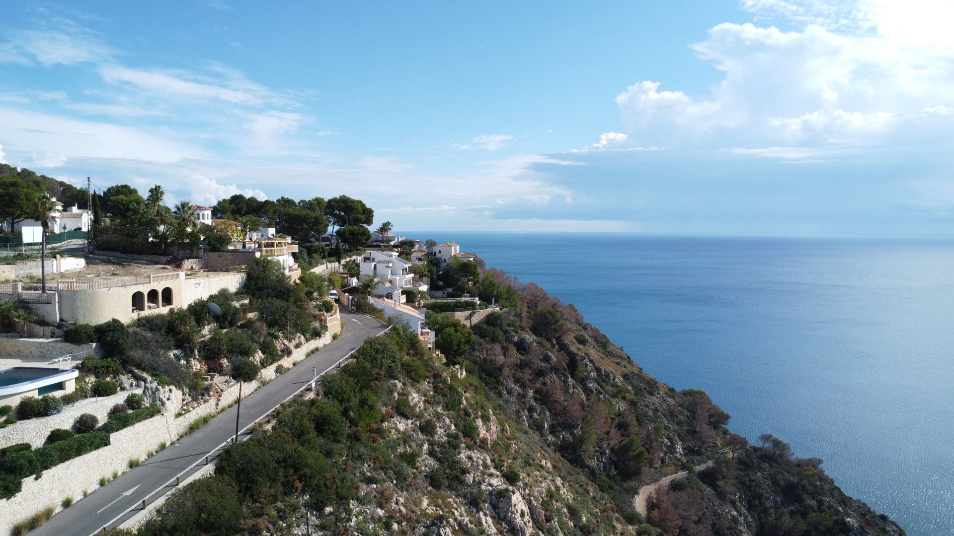 Vista aérea del entorno costero en La Granadella, mostrando la carretera de acceso y villas integradas en el acantilado frente al mar Mediterráneo.
