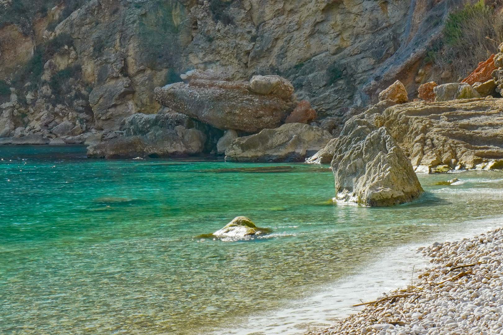 Vista de la Cala de la Granadella con sus características aguas turquesas y orilla de cantos rodados, flanqueada por acantilados escarpados en Jávea.