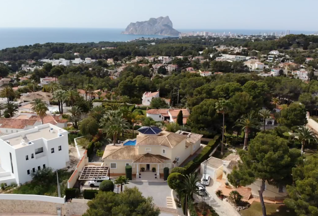 Vista aérea de la villa con arquitectura tradicional, cúpula azul y amplio acceso pavimentado, destacando las vistas al Peñón de Ifach y al mar Mediterráneo.