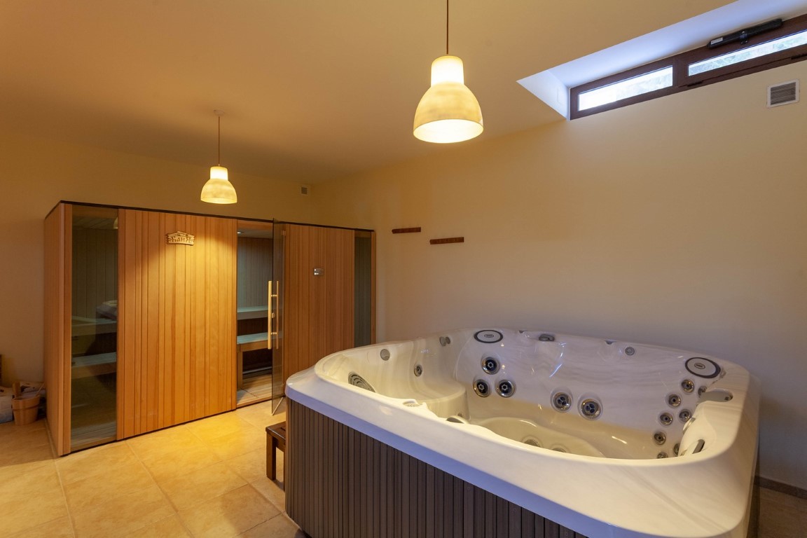 Zona de bienestar con jacuzzi de hidromasaje y sauna de madera integrada. El espacio cuenta con suelos cerámicos, iluminación cálida y una ventana superior para ventilación natural.
