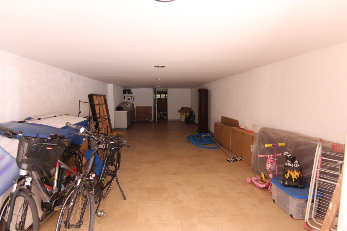 Amplio garaje de 60m2 con suelos cerámicos, paredes blancas y focos empotrados, ofreciendo un gran espacio diáfano para almacenamiento y vehículos.