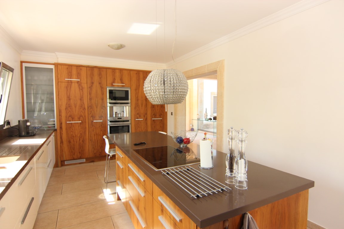 Cocina equipada con isla central, encimera técnica marrón y armarios de madera con veta vertical. Incluye electrodomésticos integrados y una lámpara de diseño esférica.