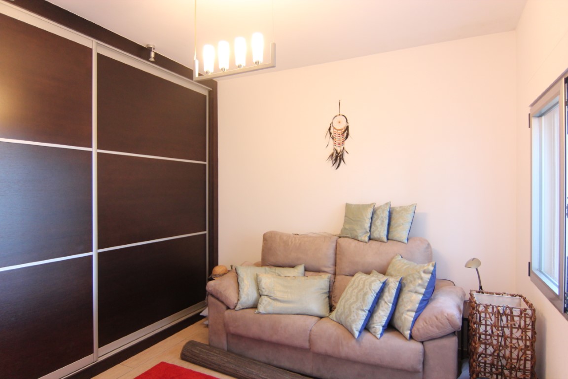 Dormitorio con armario empotrado de madera oscura y puertas correderas, acompañado de un sofá con cojines decorativos y una lámpara de techo moderna.