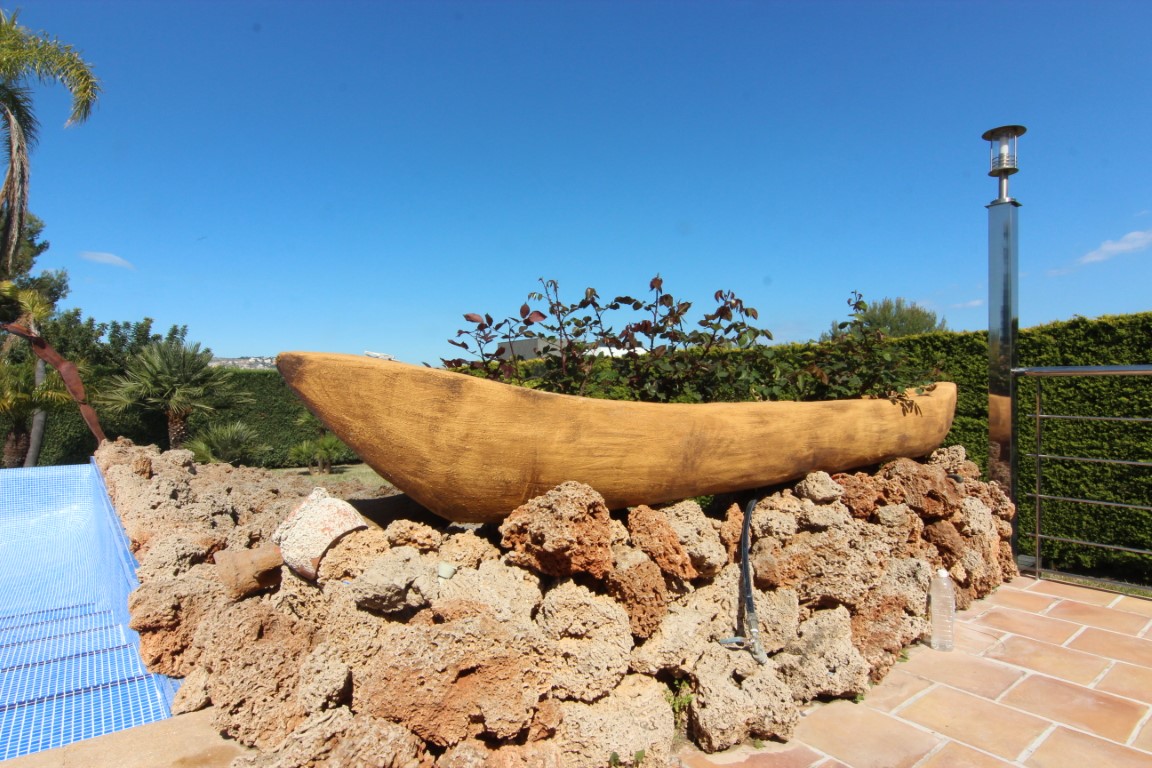 Jardinera decorativa en forma de barca sobre base de piedra natural, situada junto a la piscina y la terraza de baldosas cerámicas.