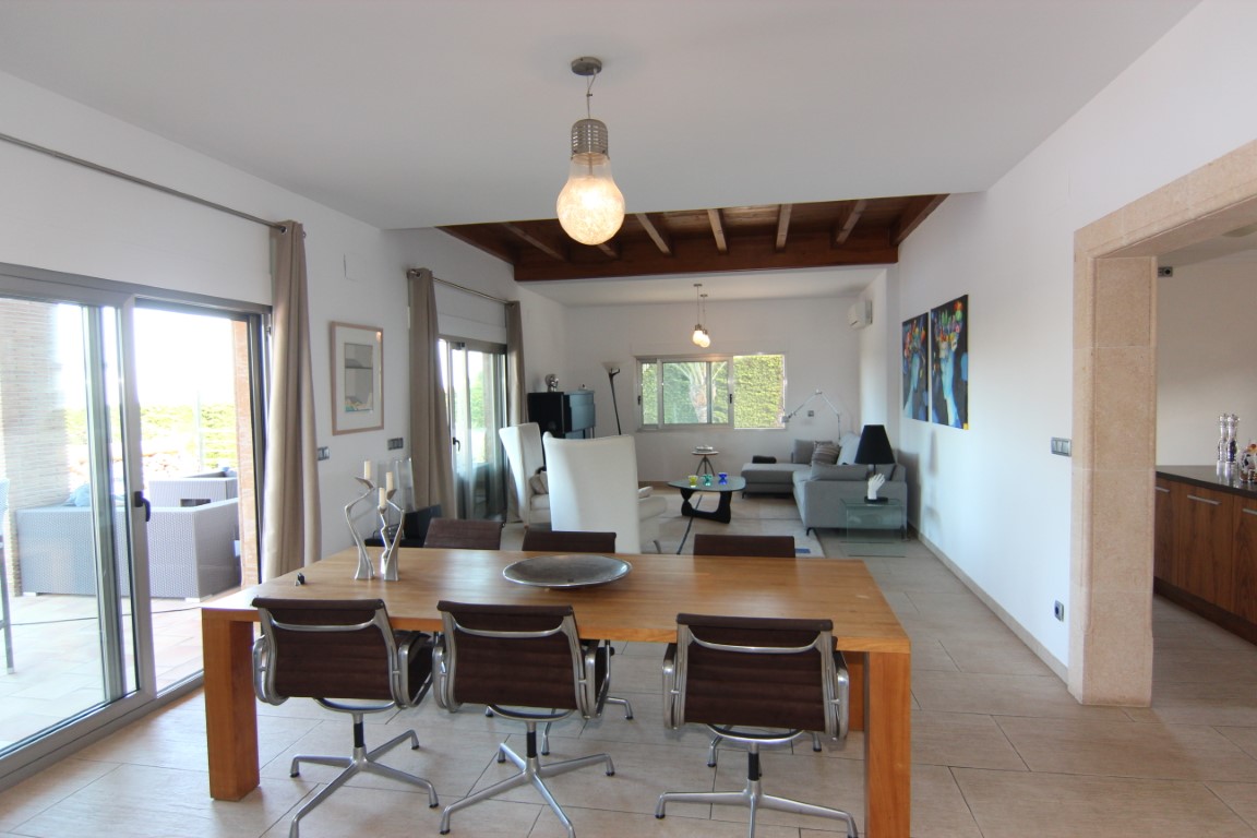 Salón comedor diáfano con techos de vigas de madera, mesa de comedor robusta y acceso directo a la terraza a través de amplios ventanales correderos.