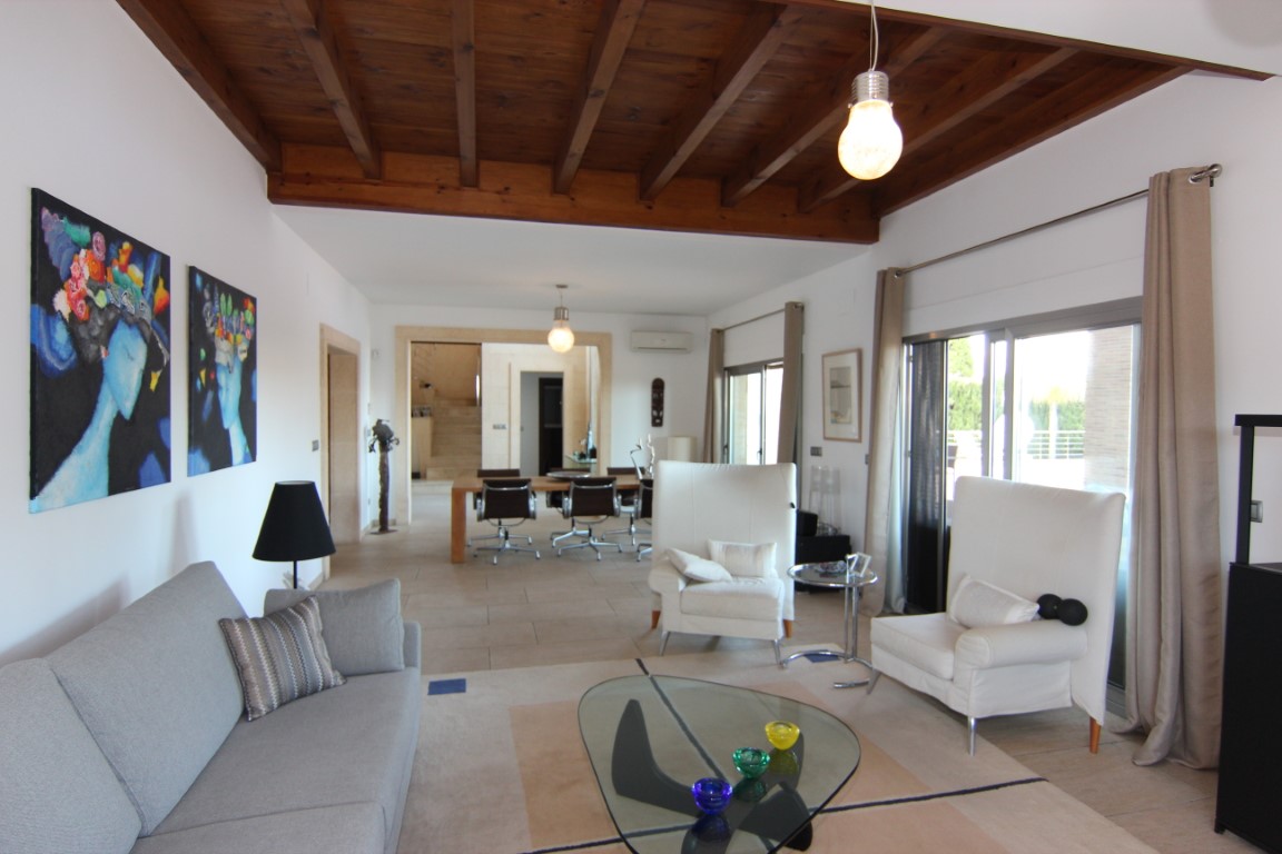 Salón luminoso con techos de vigas de madera vista, grandes ventanales correderos hacia la terraza y un diseño diáfano que conecta visualmente con el comedor.