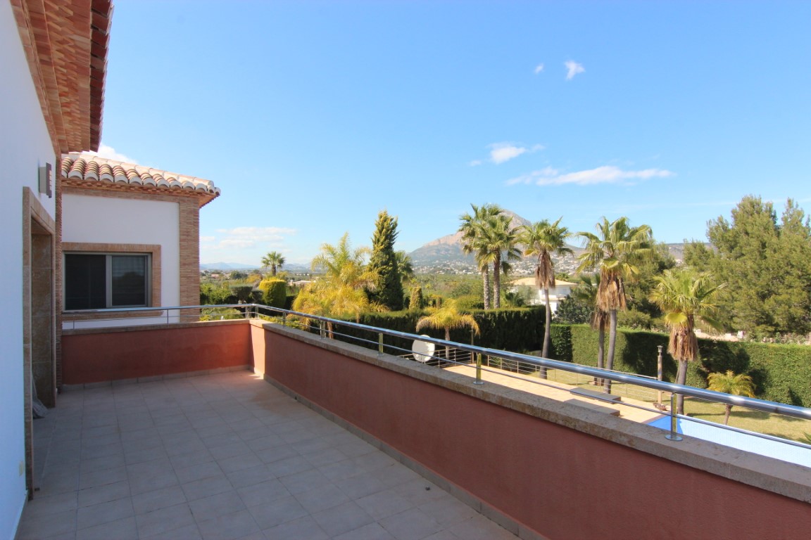 Terraza superior con suelo cerámico y barandilla de acero, con vistas panorámicas al jardín, la piscina y la silueta del Montgó en Jávea.