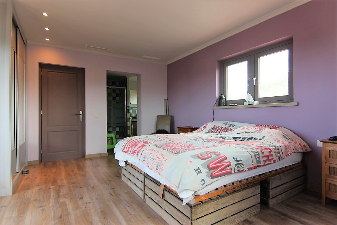 Dormitorio doble con paredes en tono lila, suelo de madera y cama sobre base de palets. Incluye armario empotrado, iluminación empotrada y acceso al baño.