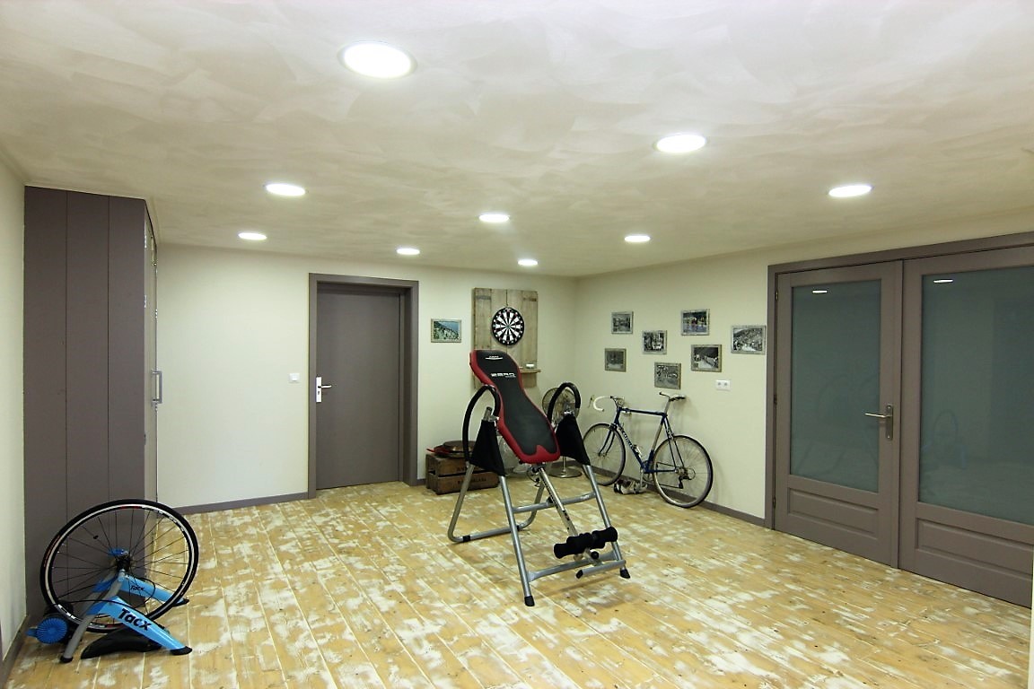 Gimnasio en el sótano con suelo de madera clara, iluminación empotrada y espacio para equipamiento deportivo, incluyendo bicicletas y una tabla de inversión.