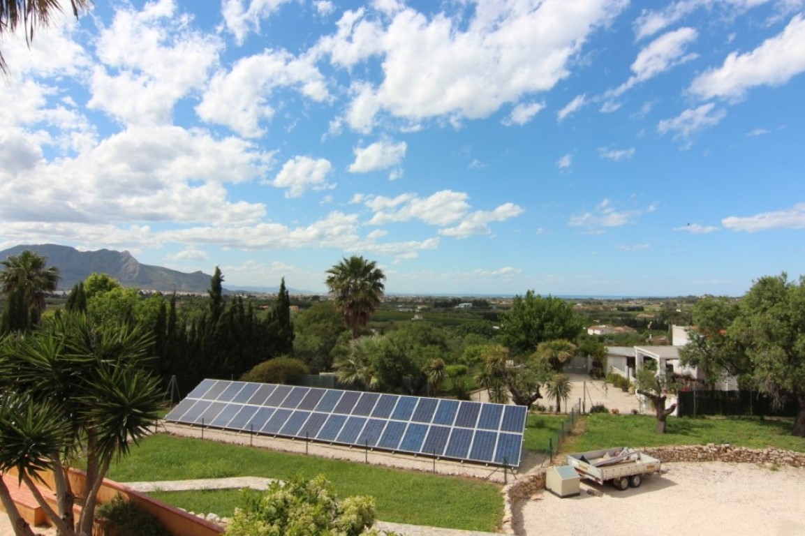 Vista panorámica de la parcela con instalación de paneles solares fotovoltaicos, rodeada de vegetación mediterránea y vistas despejadas a las montañas y al mar.