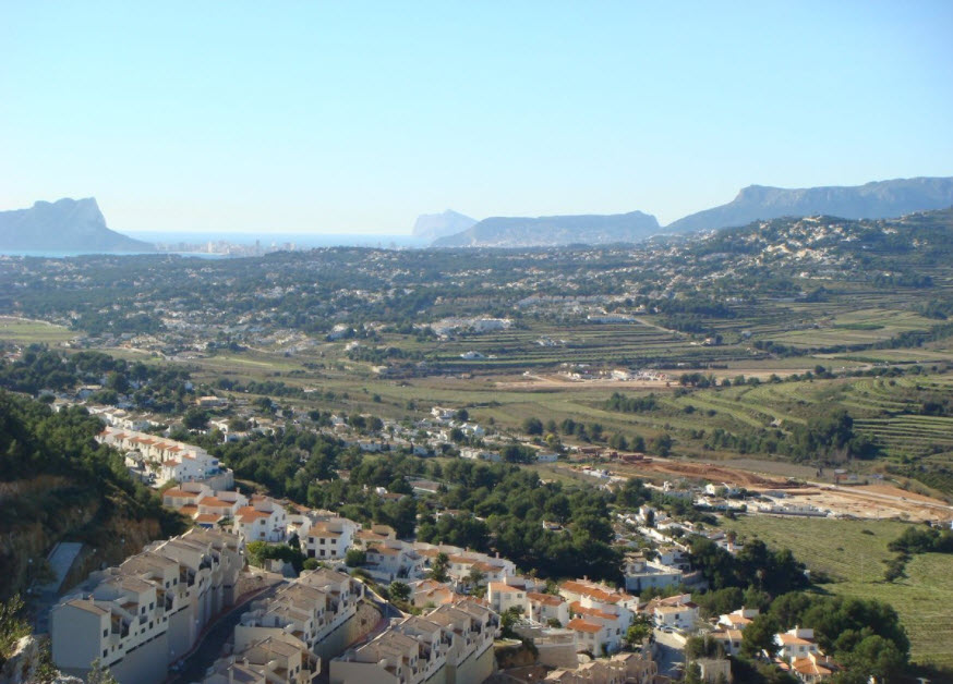 Vista panorámica desde Benitachell hacia el valle y el mar, destacando el relieve montañoso de la Costa Blanca y urbanizaciones integradas en el paisaje mediterráneo.