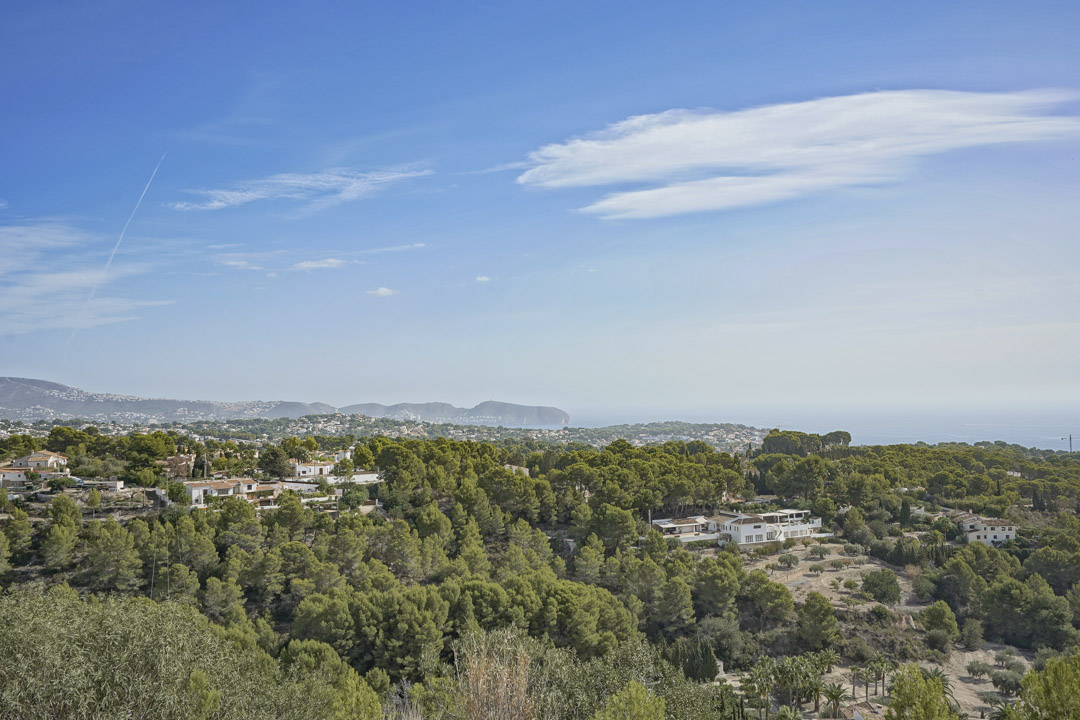 Vista panorámica desde la parcela que muestra un denso pinar mediterráneo, villas residenciales y el horizonte del mar bajo un cielo despejado.