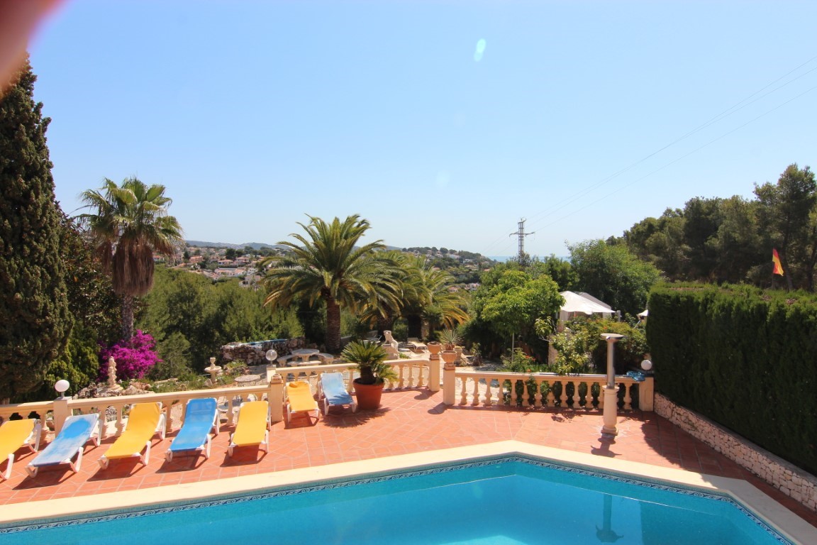 Amplia terraza con piscina, pavimentada en terracota y equipada con tumbonas, rodeada de jardines mediterráneos y vistas despejadas hacia la costa.