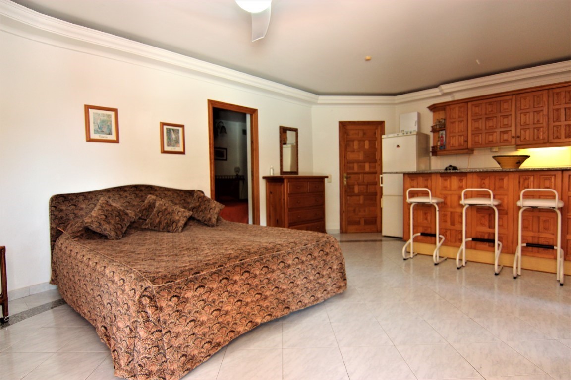 Apartamento independiente con cama doble, cocina integrada con barra de madera y taburetes, suelos de baldosa y mobiliario de madera clásica.