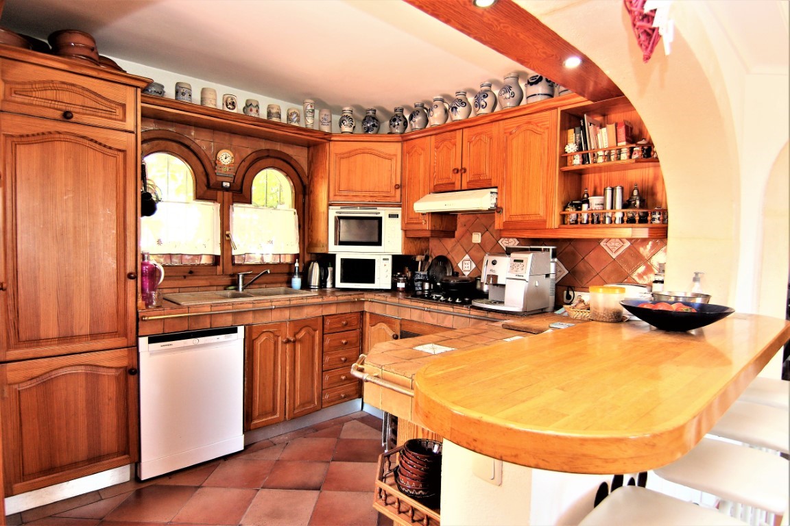 Cocina rústica con armarios de madera maciza, encimeras de azulejo y barra de desayuno. Incluye electrodomésticos integrados y ventanas tradicionales con arco.