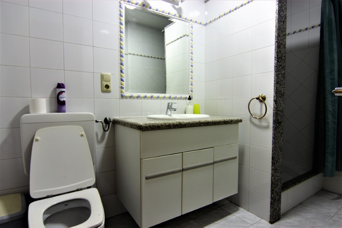 Cuarto de baño con lavabo sobre encimera de granito, espejo con marco decorativo y ducha independiente con marco de piedra natural y cortina.