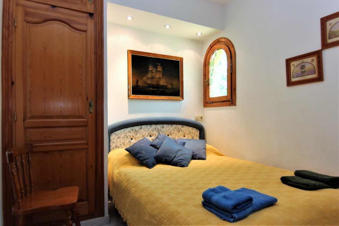 Dormitorio acogedor con armario de madera integrado, ventana de arco tradicional e iluminación empotrada sobre el cabecero decorado.