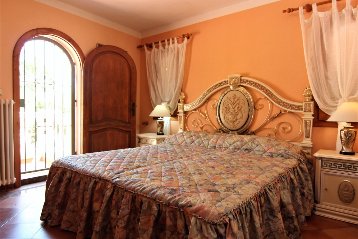 Dormitorio con cabecero ornamental de estilo clásico, paredes en tono melocotón y acceso directo al exterior mediante una puerta de madera en arco.