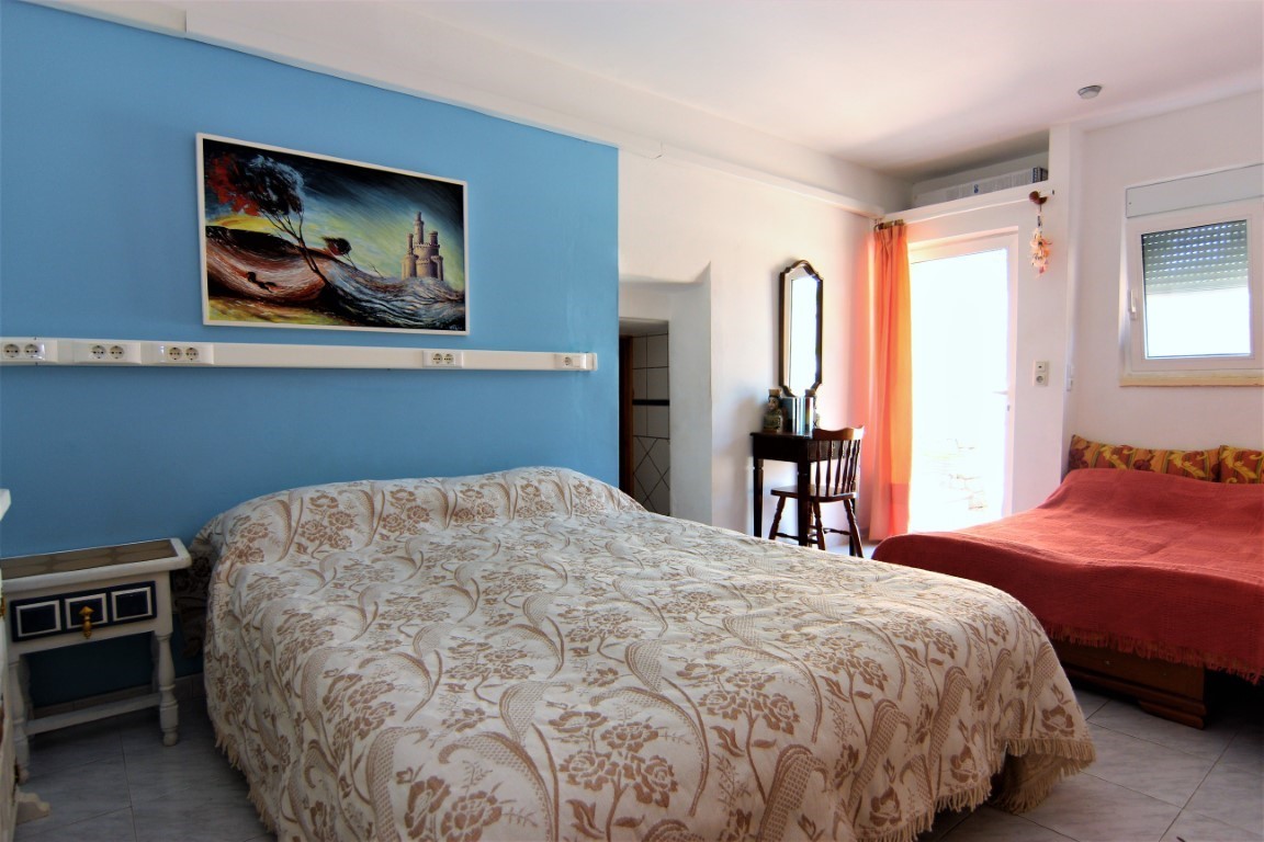 Dormitorio luminoso con pared de acento azul, cama doble con colcha estampada y cama individual adicional. Incluye escritorio de madera, suelo cerámico y acceso directo al exterior.